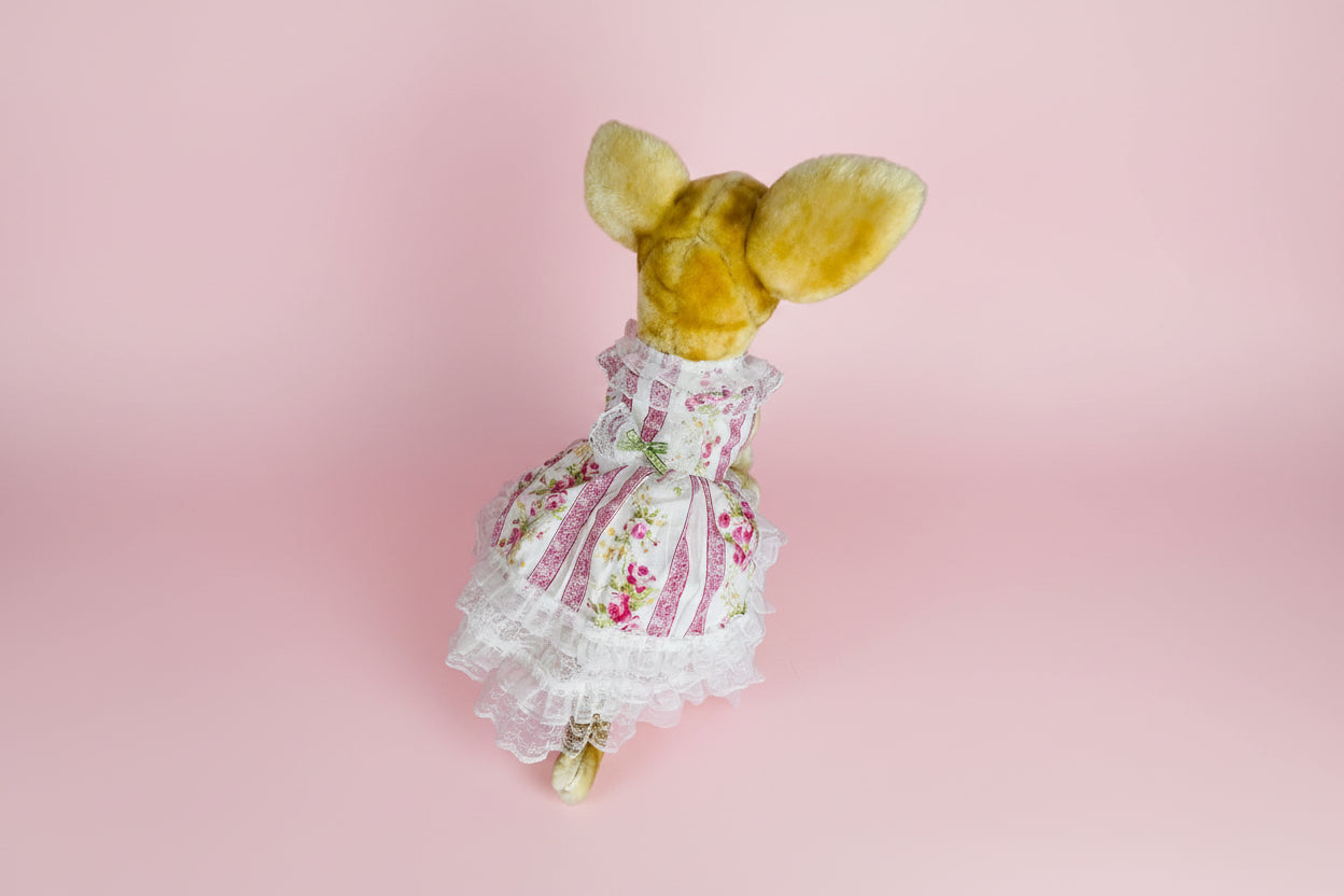 Stuffed animal wearing a floral dress on a pink background