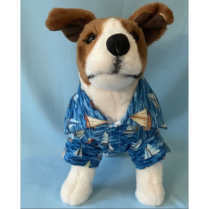 Stuffed dog toy wearing a blue outfit with sailboat pattern on a white background