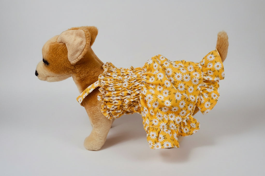 Stuffed dog toy wearing a yellow floral dress on a white background