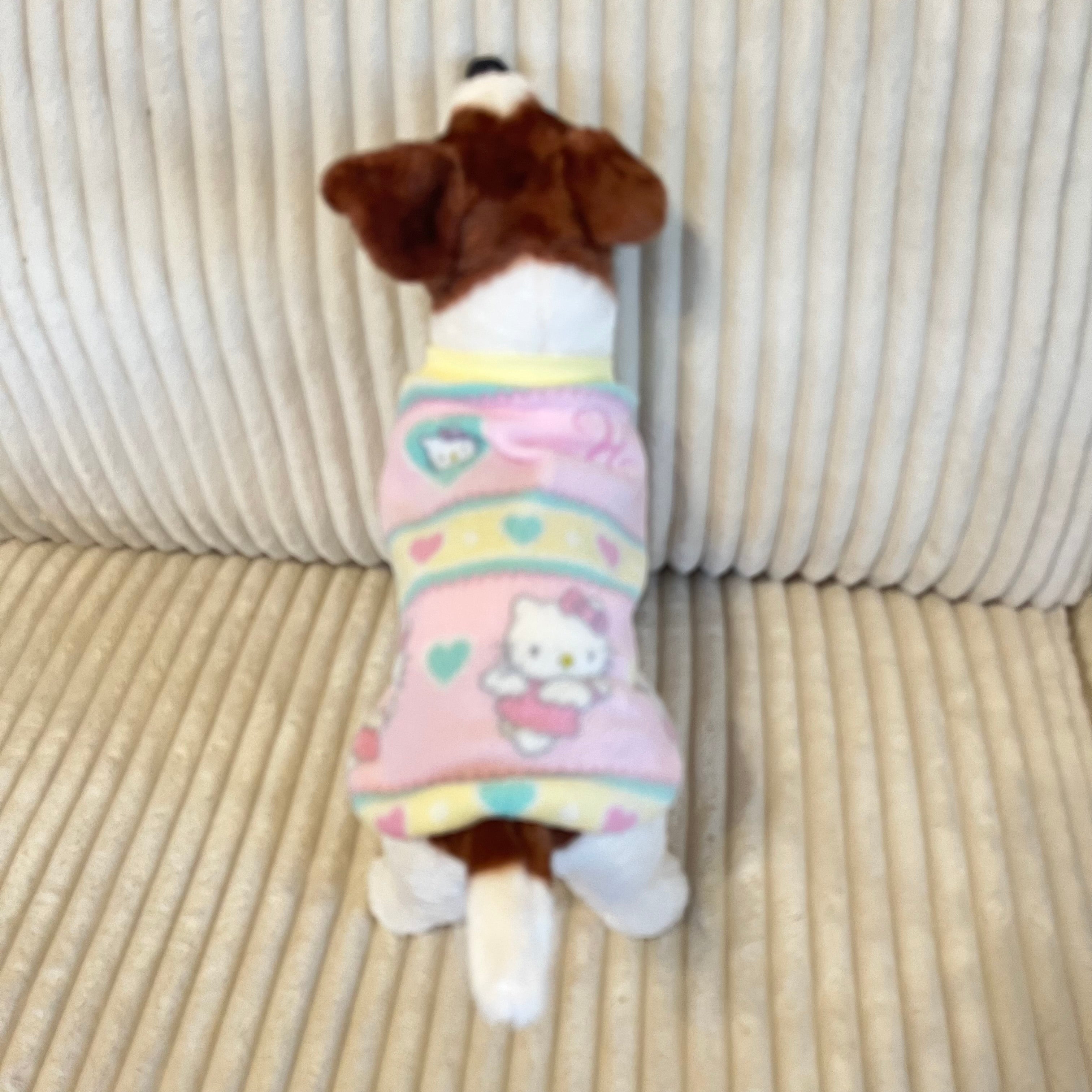 Small dog wearing a colorful long sleeve fleece hello kitty dog  sweater on a beige couch.