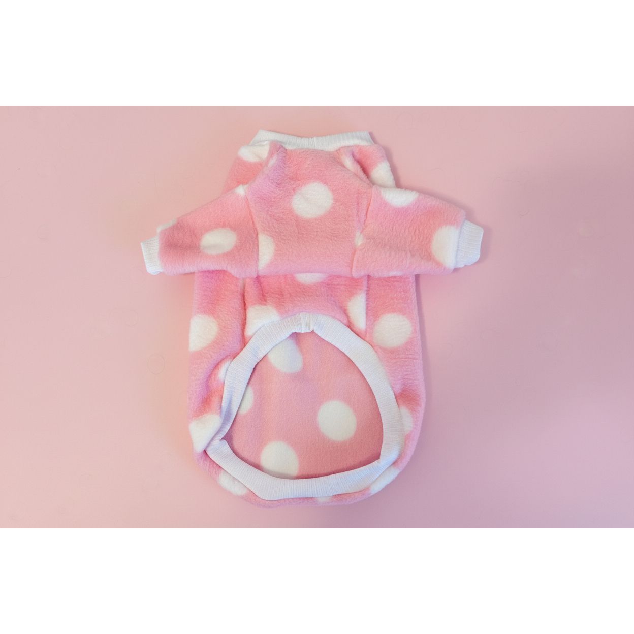 Pink fleece dog coat with white polka dots on a beige textured background