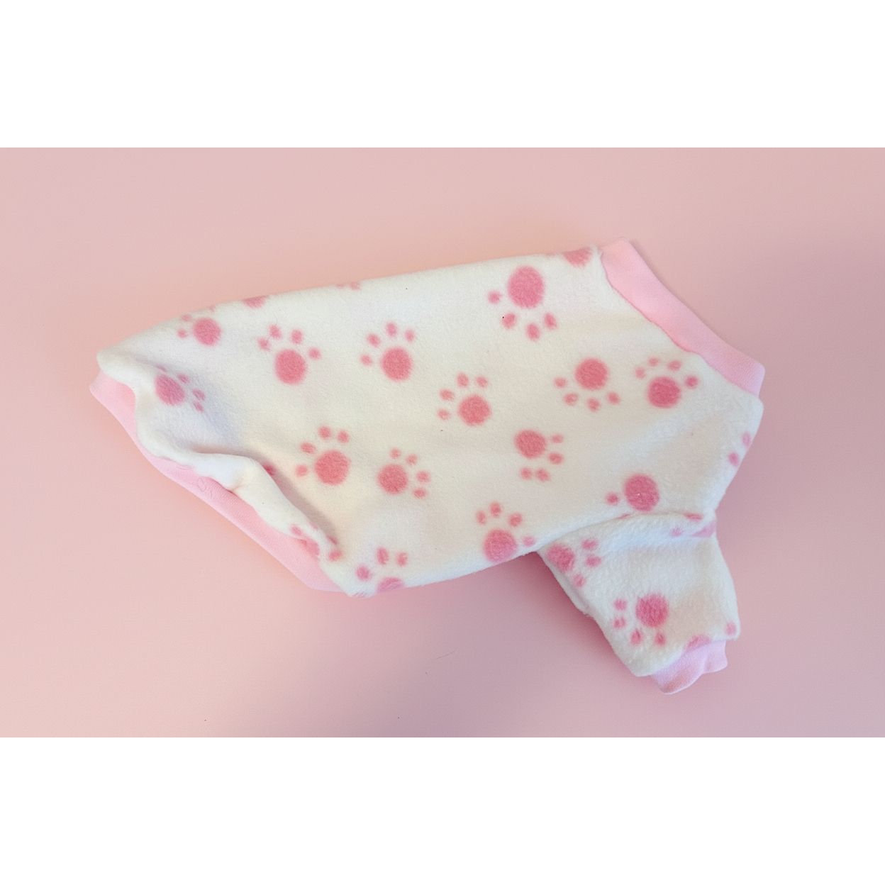 Small dog coat with pink paw prints on a textured beige surface