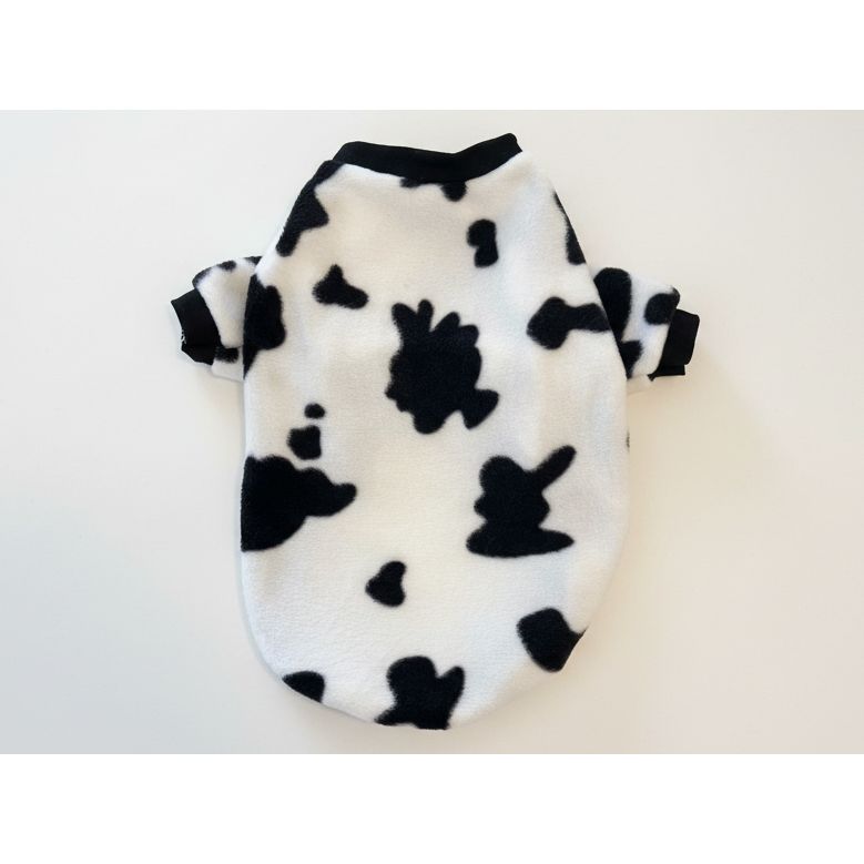 Black and white cow patterned dog sweater on a beige marble background