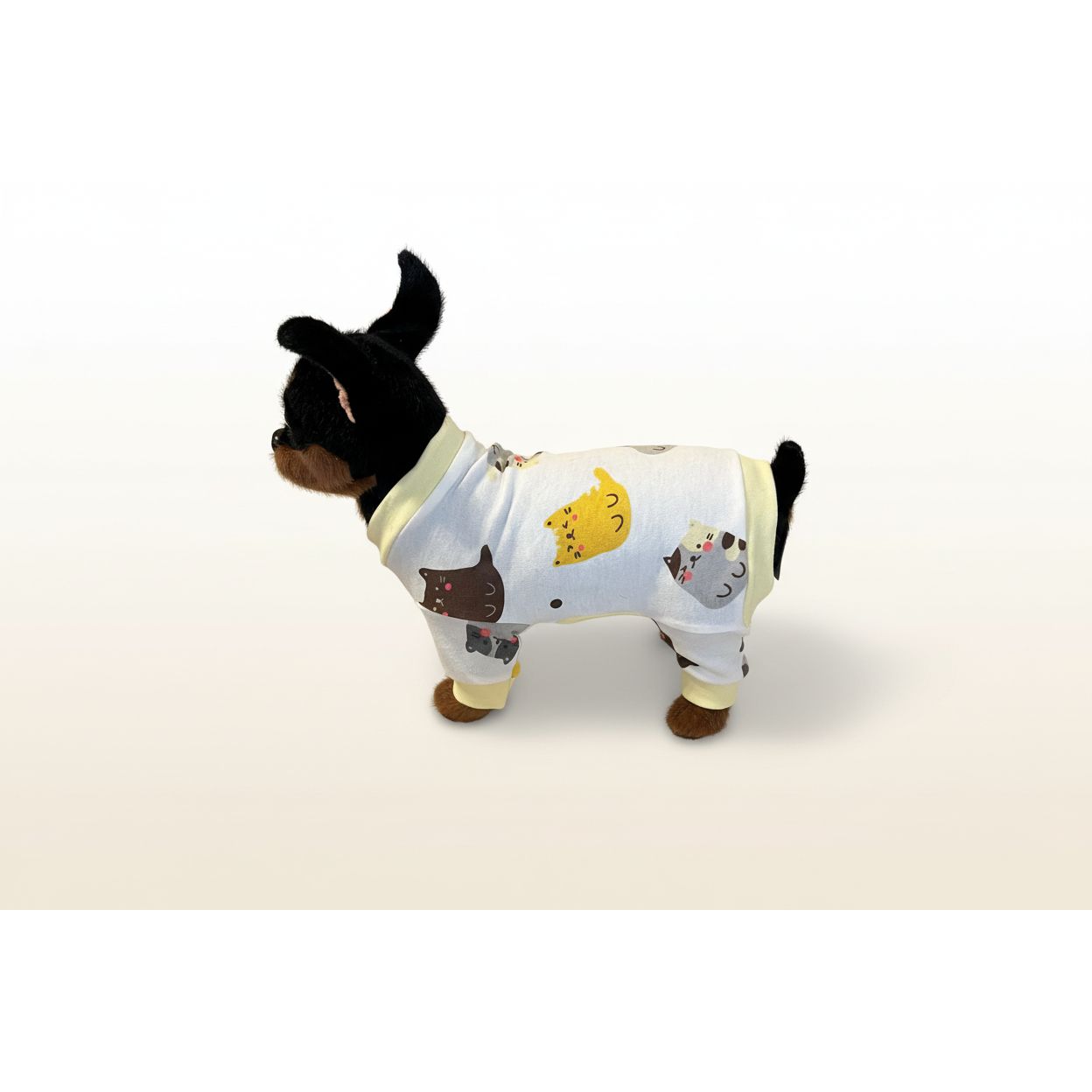 Dog wearing a white onesie with cartoon cat designs on a beige couch.