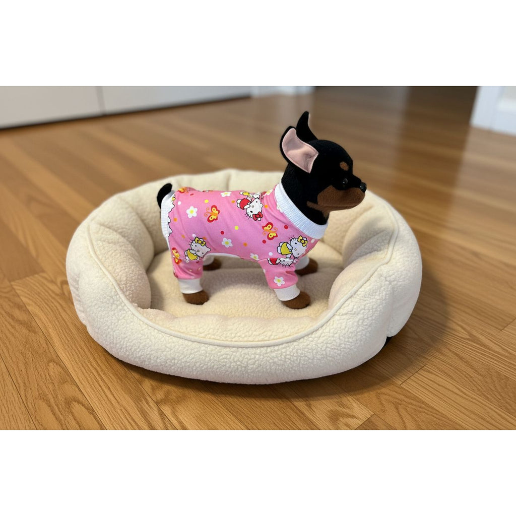 Small dog wearing a pink outfit with cartoon characters on a beige couch