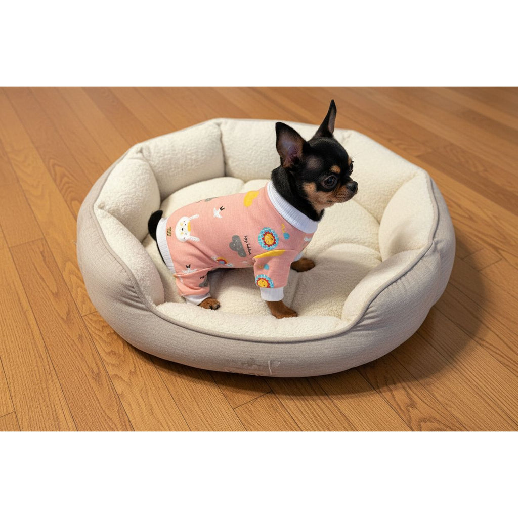 Small dog wearing a pink outfit with animal prints on a beige couch.
