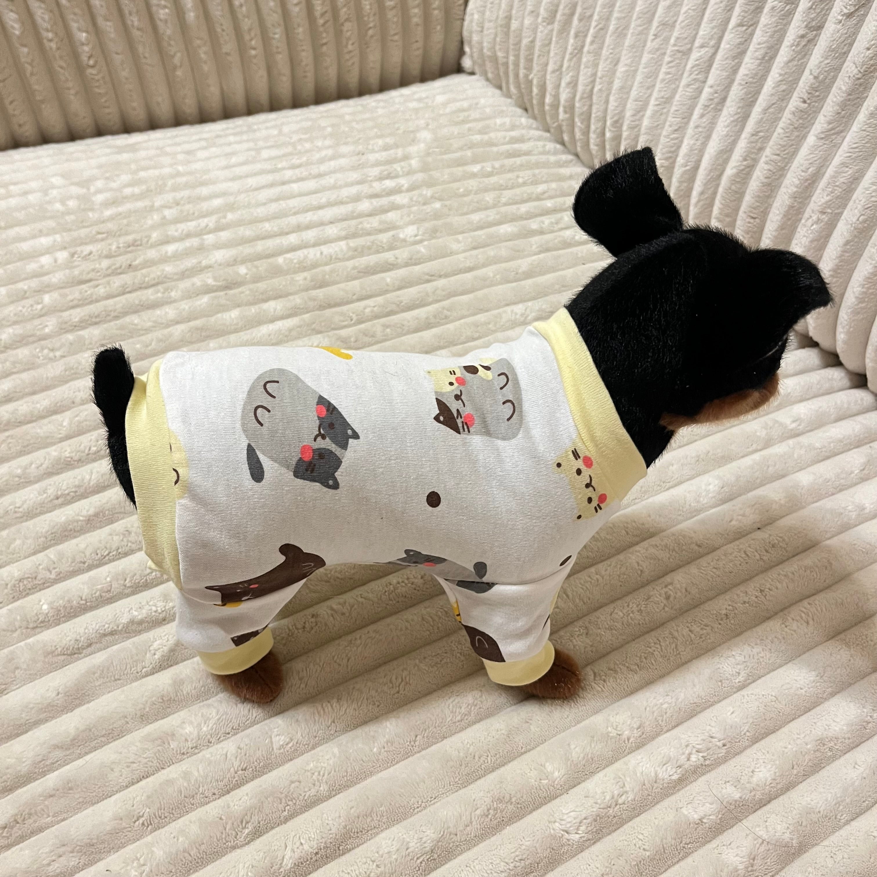 Small dog wearing a white onesie with black cat illustrations on a beige couch.
