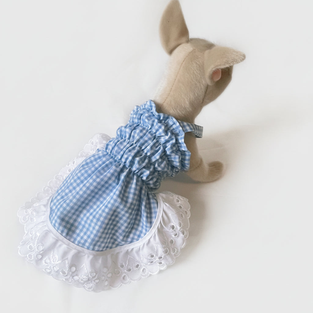 Stuffed animal wearing a blue checkered dress with white lace trim on a white background