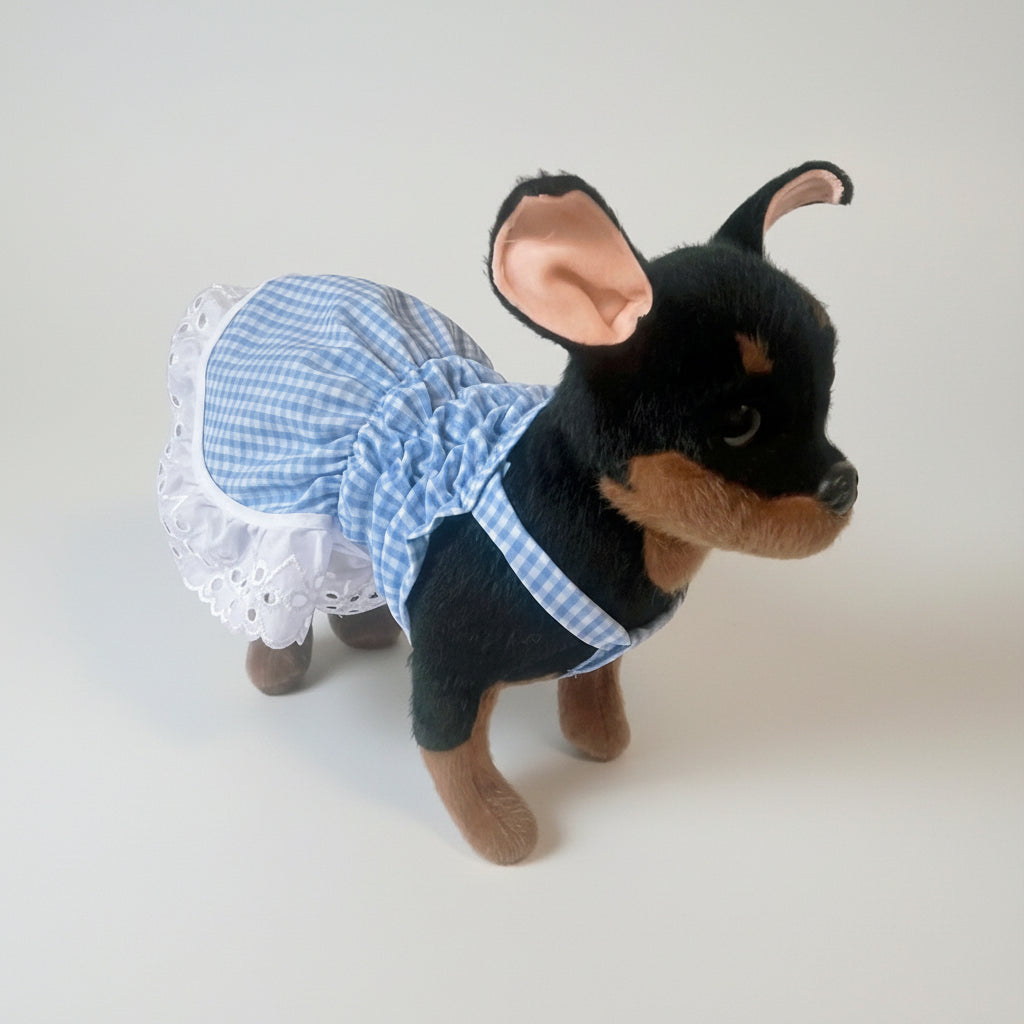 Stuffed dog toy wearing a blue checkered dress on a white background