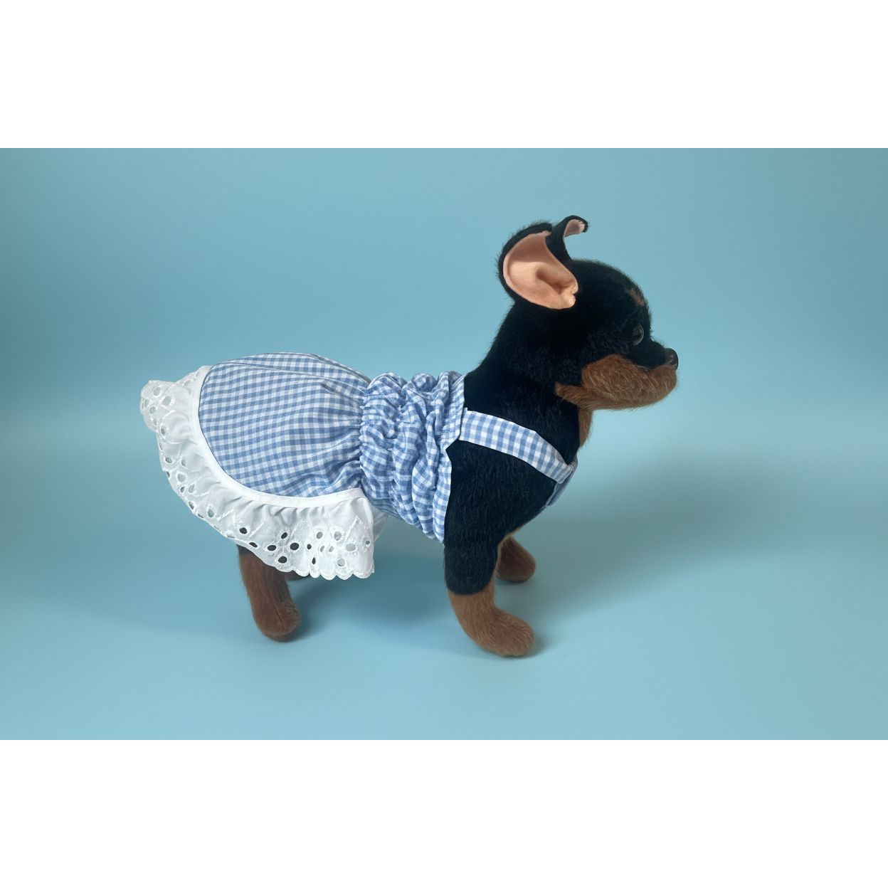 Stuffed dog toy wearing a blue checkered dress with white lace trim on a white background