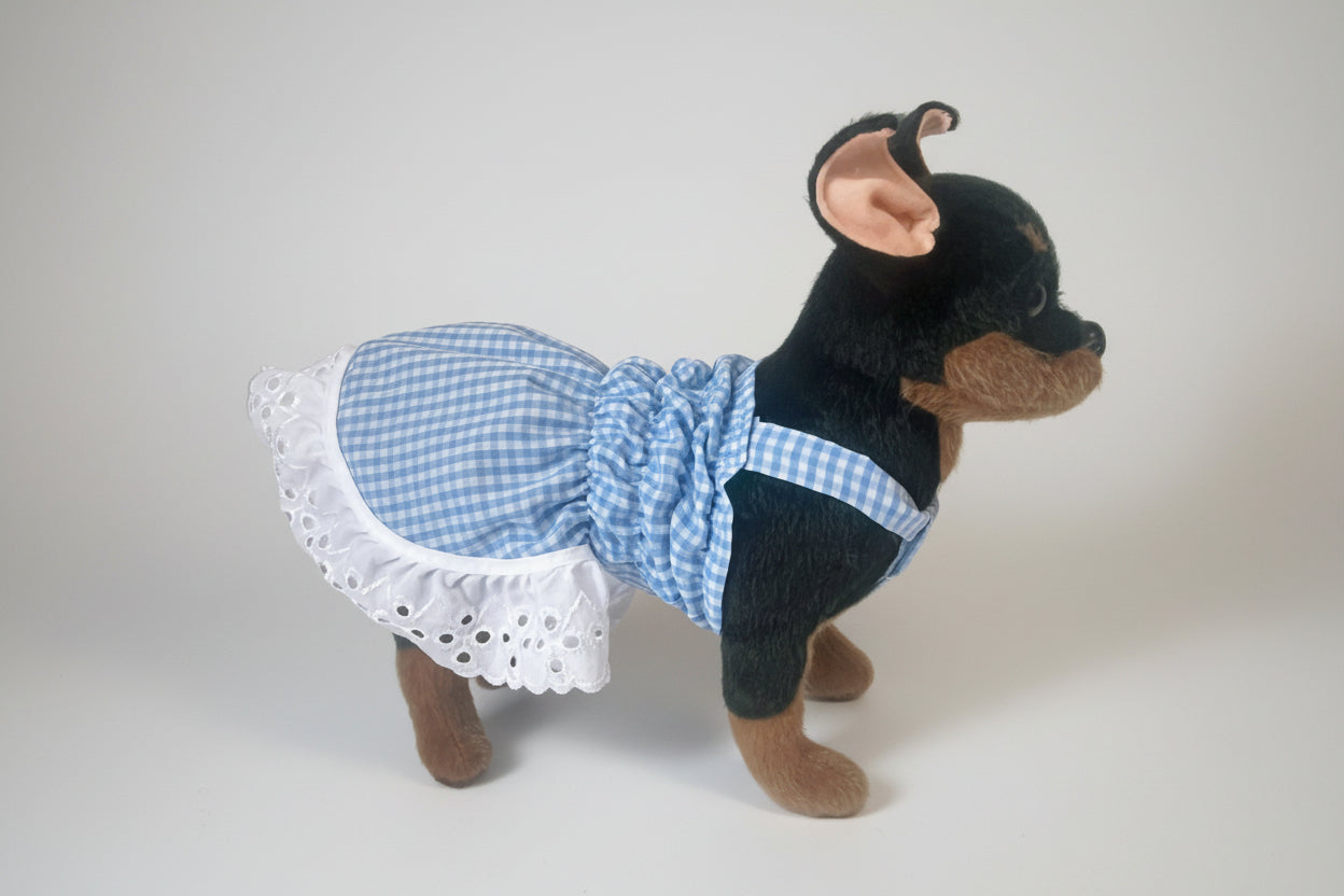 Stuffed dog toy wearing a blue checkered dress with white lace trim on a white background