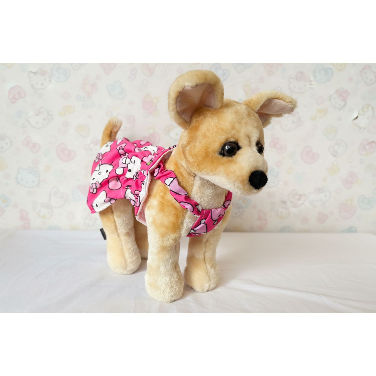 Stuffed dog toy wearing a pink Hello Kitty outfit on a white background