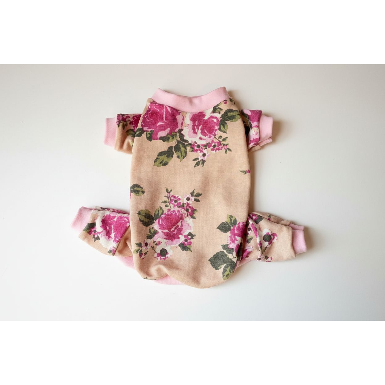 Floral four leg dog pajamas with pink accents on a beige surface