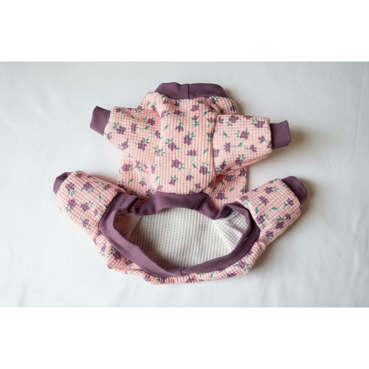 Floral-patterned dog pajamas with purple accents on a beige surface