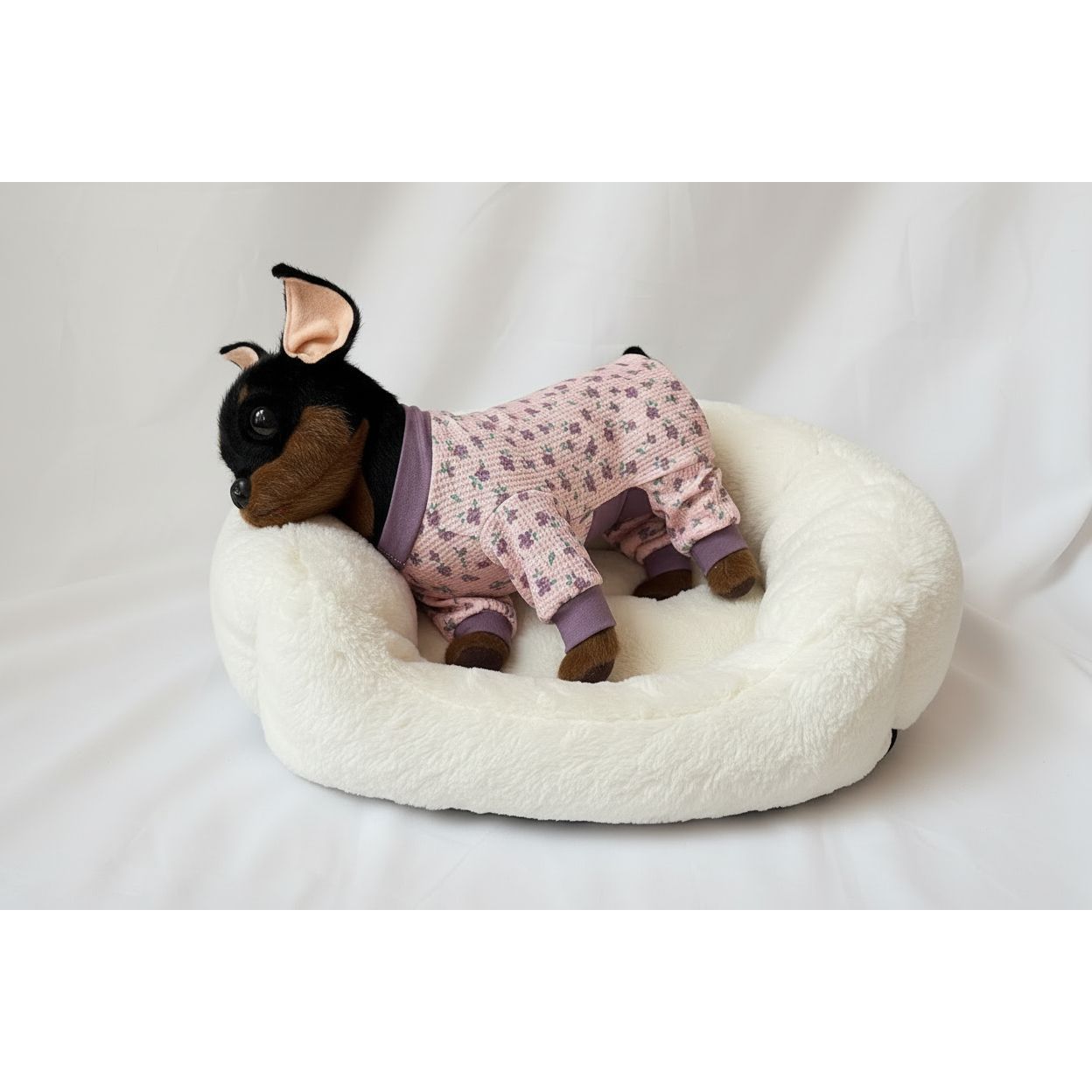 Stuffed dog toy wearing a pink floral onesie on a white background