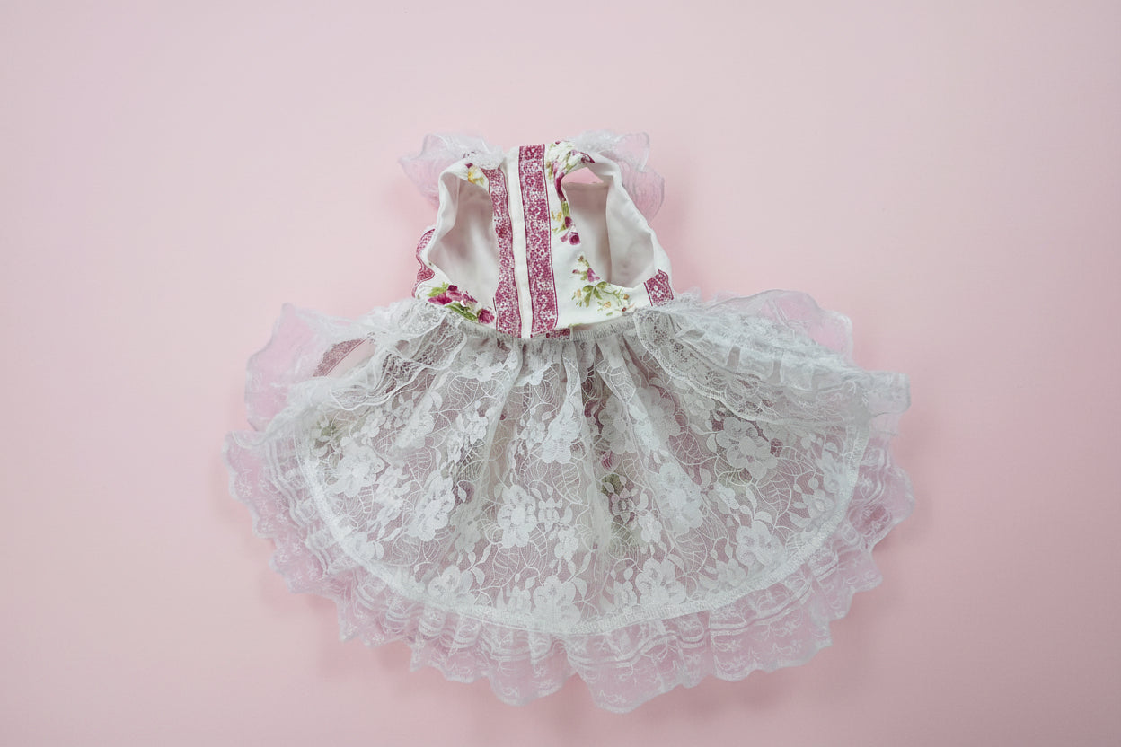 White lace dog dress with floral straps on a pink surface